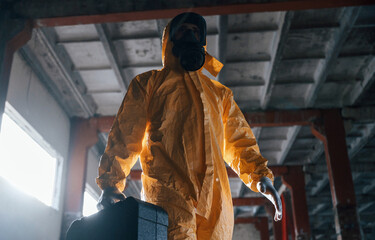 Walking with hard case. Man dressed in chemical protection suit in the ruins of the post...