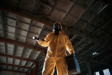 Using the flashlight. Man dressed in chemical protection suit in the ruins of the post apocalyptic building