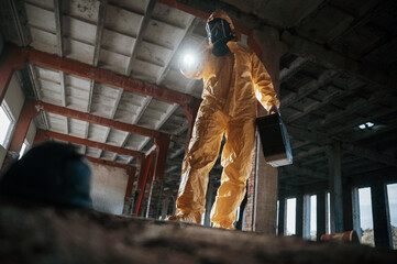 Looking below at the object. Man dressed in chemical protection suit in the ruins of the post apocalyptic building