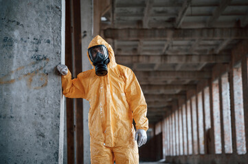 Leaning on the wall. Man dressed in chemical protection suit in the ruins of the post apocalyptic...