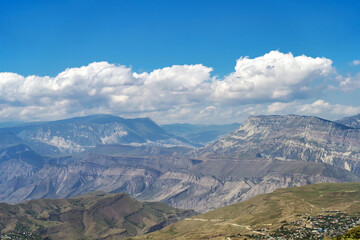 Fototapeta premium Beautiful sunny day in mountain valley and mountainous countryside landscape in summer. Mountain range under cloud blue sky. Beautiful view on mountains valley between high peaks.