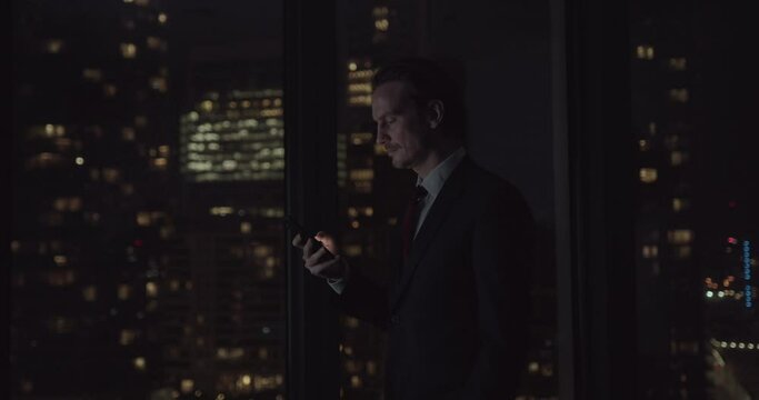 Adult Male using Smart phone Working Late in Office with City Skyline
