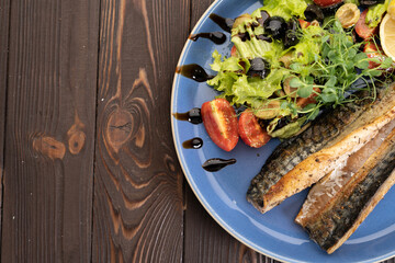 Grilled fish fillet on plate with lemon and green salad on wooden background, top view. Restaurant menu