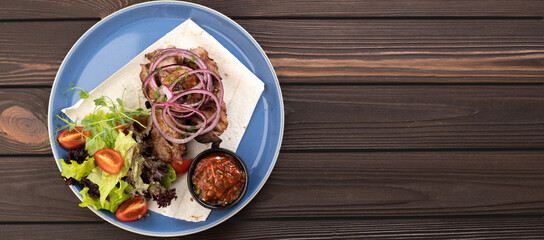 grilled kebab with sauce and vegetables on a plate on a wooden background, top view