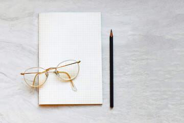 white round frame eyeglasses on the checked notebook with pencil on white background working and journal writing concept ( stationary)