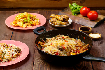 Funchoza with chicken and vegetables in teriyaki and oyster sauce in a frying pan on a covered wooden table.