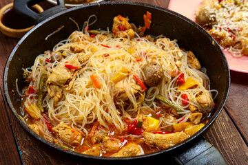 Funchoza with chicken and vegetables in teriyaki and oyster sauce in a frying pan on a wooden table with food.