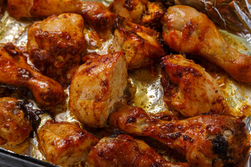 Baked chicken legs and breasts in sauce and spices in foil close-up.