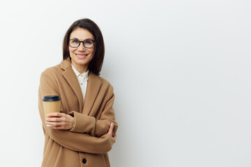 beautiful stylish woman in black glasses and a beige coat stands with her arms crossed on her chest and holds a glass of coffee.Horizontal portrait with empty space for inserting advertising text