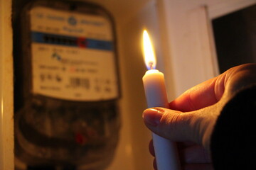 Candle in hand shines in the dark near the electricity meter during a power outage at home. City,...