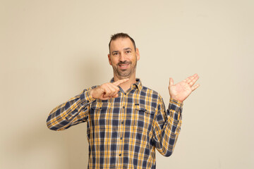 Portrait of positive bearded latin man wearing a plaid shirt isolated over beige background, points with his finger at something imaginary on his palm.