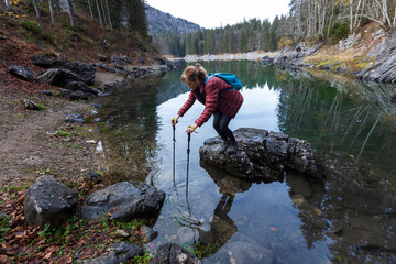 Woman Hiker Trying to not Step into Lake Water After Posing on a Rock into it Helping Herself with Hiking Poles