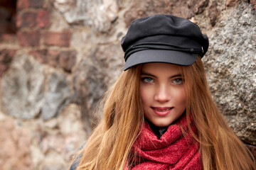 Girl in a black cap with a red scarf against a brick wall
