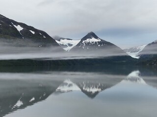 Beautiful scenery of a lake with the reflection of snowy mountains in the water on a foggy day