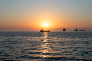 Fototapeta premium Beautiful orange sunset over the sea with a silhouettes of ships and soft selective focus. Beauty of nature concept