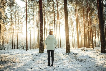 Naklejka premium Woman in a white puffer jacket against the background of snow-covered trees on a sunny day.