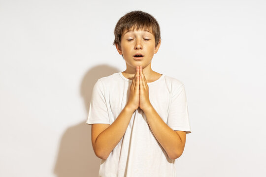 a teenager prays with his eyes closed. hard light, white background.