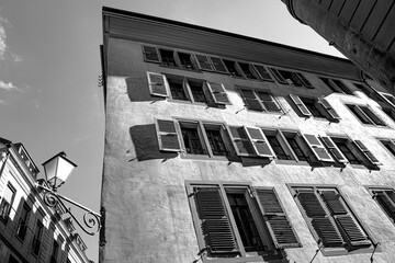 Low angle grayscale shot of an antique building in Geneva with whitewashed walls and open shutters