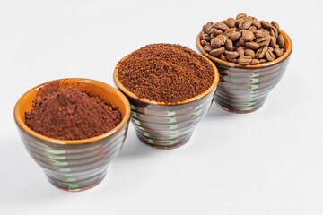 three small saucers with coffee beans, ground coffee and cocoa on a white background.