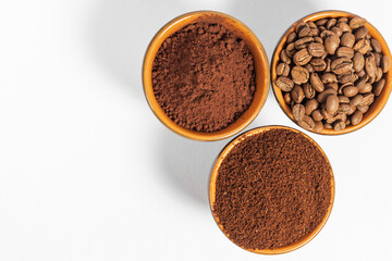 Cups with roasted coffee beans and ground coffee, white background and copy space.
