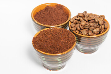 Cups with roasted coffee beans and ground coffee, white background and copy space.