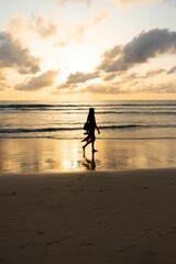 Vertical shot of the silhouette of a woman walking along the beach at sunset.