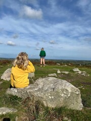 Vertical shot of a female sitting on a rock in a field on the blurred background of another female