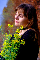 Naklejka premium Beautiful young girl in a black dress with green wildflowers on the photo of the autumn forest