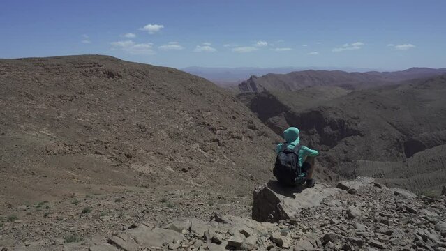 Man sitting on the edge of the cliff, enjoying the view of mountains. Todra Gorge, Morocco.