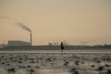 Person walking on the beach with a factory in the background in Dublin