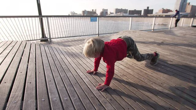 5 years old caucasian boy is having fun doing exercices on the quay plank floor at Coney island, NYC, USA. Autumn. Cool weather, the boy is in red sweater.