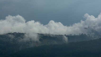 góry porośnięte lasem, mgła i niskie białe chmury, ciemne niebo - obrazy, fototapety, plakaty