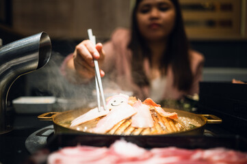 Fototapeta na wymiar Woman Holding chopsticks, eating shabu, suki, hot pot at a Japanese restaurant. selective focus