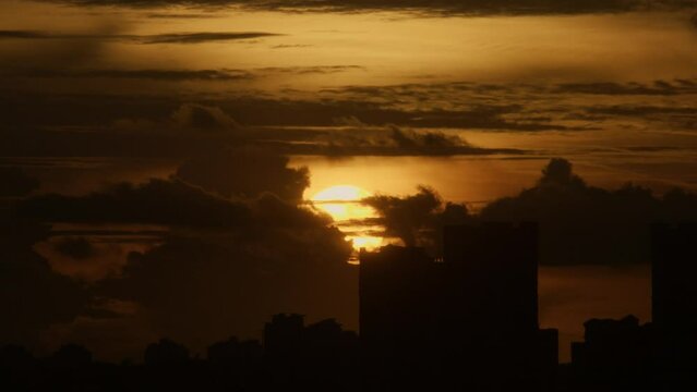 Timelapse of the clouds in the sky at soft sunset over the silhouette of the buildings