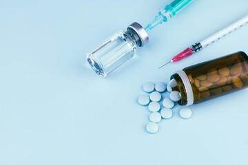 Closeup of pills and a container with a syringe on blue background