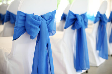 a row of chairs at a wedding banquet with white cover and decorated with blue bows