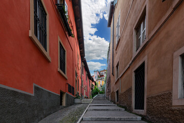 Fototapeta na wymiar Narrow little street with stairs in Verona, Italy red and orange walls of buildings and wooden windows. City street with old architecture and green flowers.