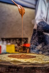 Vertical closeup of a spoon with chocolate pouring down to the hot blini
