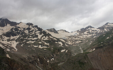 The high snow-capped peaks of the mountains in the Elbrus region in the North Caucasus and the cloudy sky with a blurred misty haze over the peaks and the space for copying
