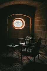 Two chairs and a table on a rug in a room with stone walls and a stained glass window