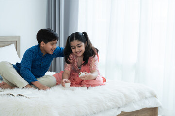 Obraz na płótnie Canvas Happy Indian family, brother and sister with traditional clothes playing fun game together, two children boy and girl sitting talking on bed at home, sibling relationship concept