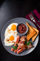 Full English Breakfast on dark table sausage eggs bean bacon tomatos mushroom