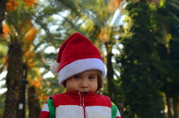 Little Santa Claus in a red hat and elf costume. Boy on vacation, tropical resort, Christmas at sea. Concept: travel, vacation, family trip