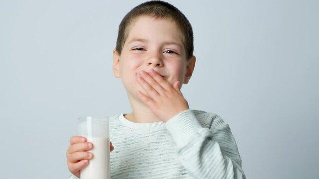 A handsome 5-year-old boy holds a glass of fermented milk in a glass on a white background