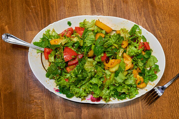Healthy vitamin salad of green leaves and various vegetables in a large white plate.