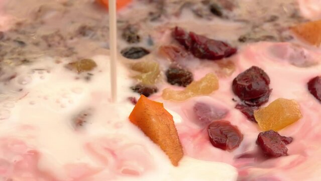 High angle view pouring strawberry milk into bowl of strawberry yoghurt with preserved sweet dried organic tropical fruit.