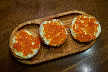 Sandwiches with red caviar on a wooden tray.
