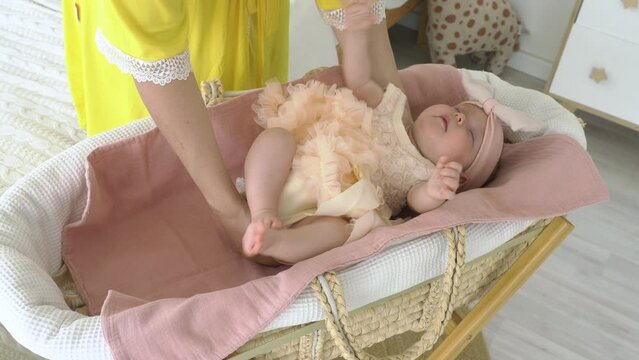 Mother putting her baby in cute dress to sleep in the vintage wicker crib in nursery