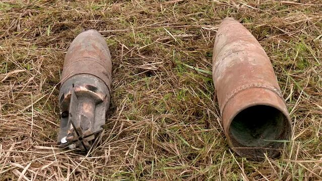 Unexploded remnants of live ammunition lie on the ground in dry grass. Demining