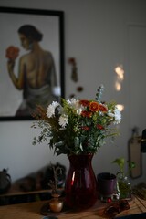 Flower vase on a wooden table with a painting of a woman in the background - vertical shot